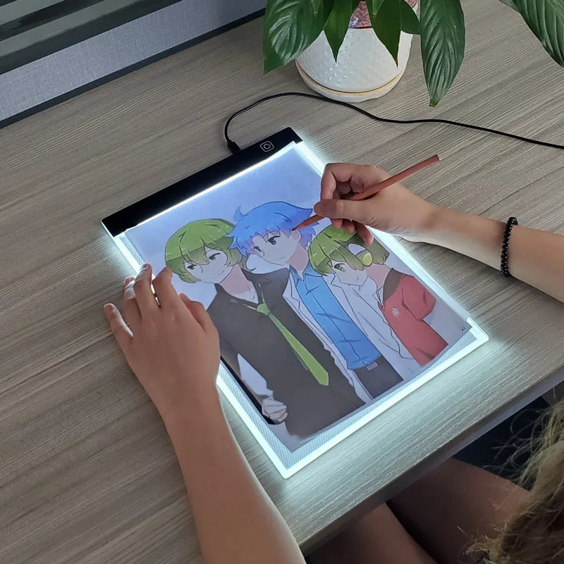 A person is drawing on an illuminated LED copy pad featuring anime-style characters.