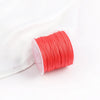 A roll of bright orange-red macrame cord for jewelry making and crafts, resting on a white cloth.