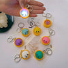 A hand holds a colorful dumpling stress relief keychain with an LED light and various other keychains.