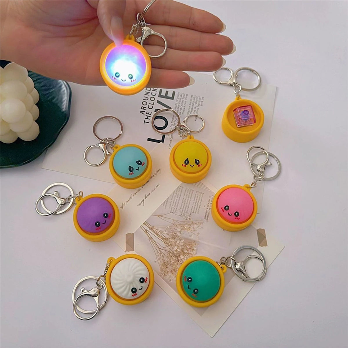 A hand holds a colorful dumpling stress relief keychain with an LED light and various other keychains.