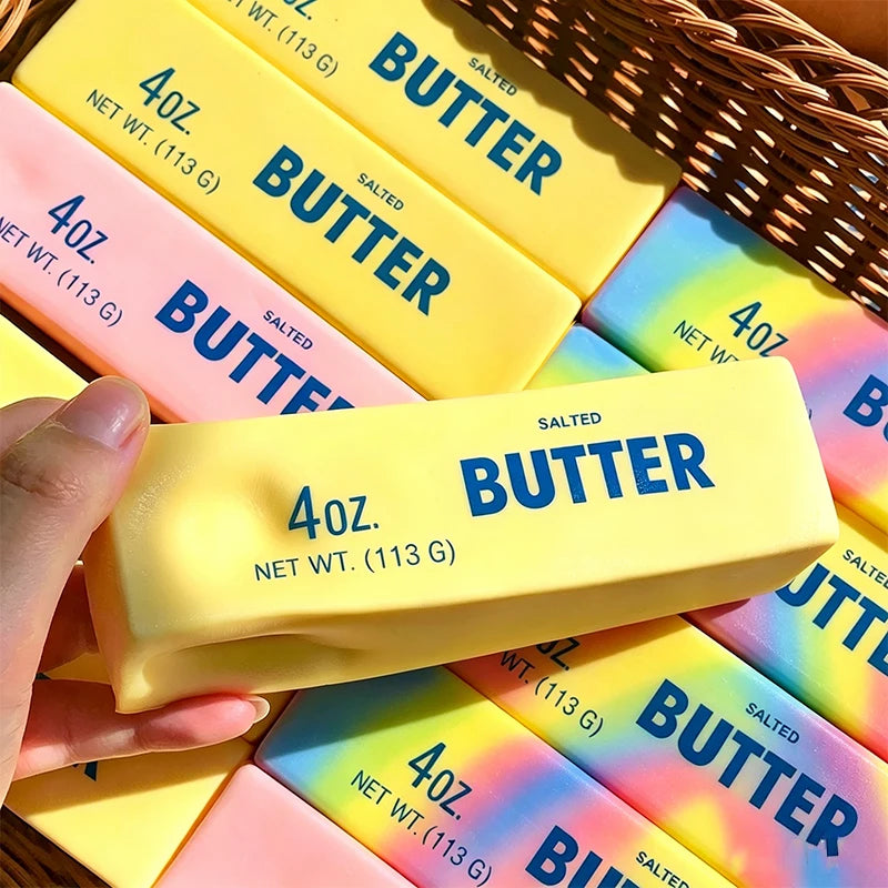 A hand holds a yellow butter stress relief toy with blue lettering against a background of other similar products.