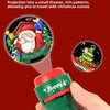 A hand holds a green flashlight with a red cap, showing a Christmas projection onto a dark surface.