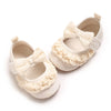 A pair of light beige soft cotton baby walking shoes with ruffled fabric bows and anti-slip soles.