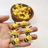 A hand holds several yellow and black silicone bee beads next to a bowl full of similar bees.