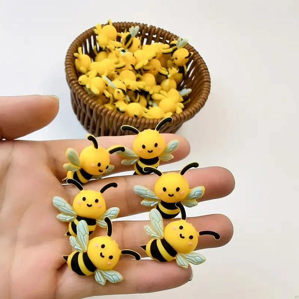 A hand holds several yellow and black silicone bee beads next to a bowl full of similar bees.