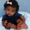 A baby with curly hair wearing a dark blue top is sitting on a white fluffy surface.