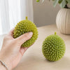 A hand holds a bright green, textured durian squeeze toy against a light background.
