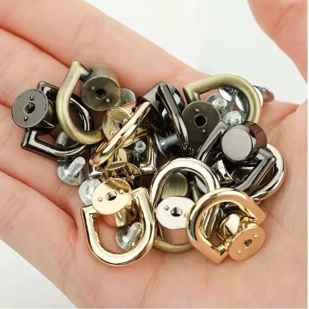 A collection of D-shaped metal bag handles and hardware including rings, clasps, and screws held in a person's hand.