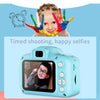 A young girl is posing for a selfie with colorful handprints in front of a small blue digital camera.