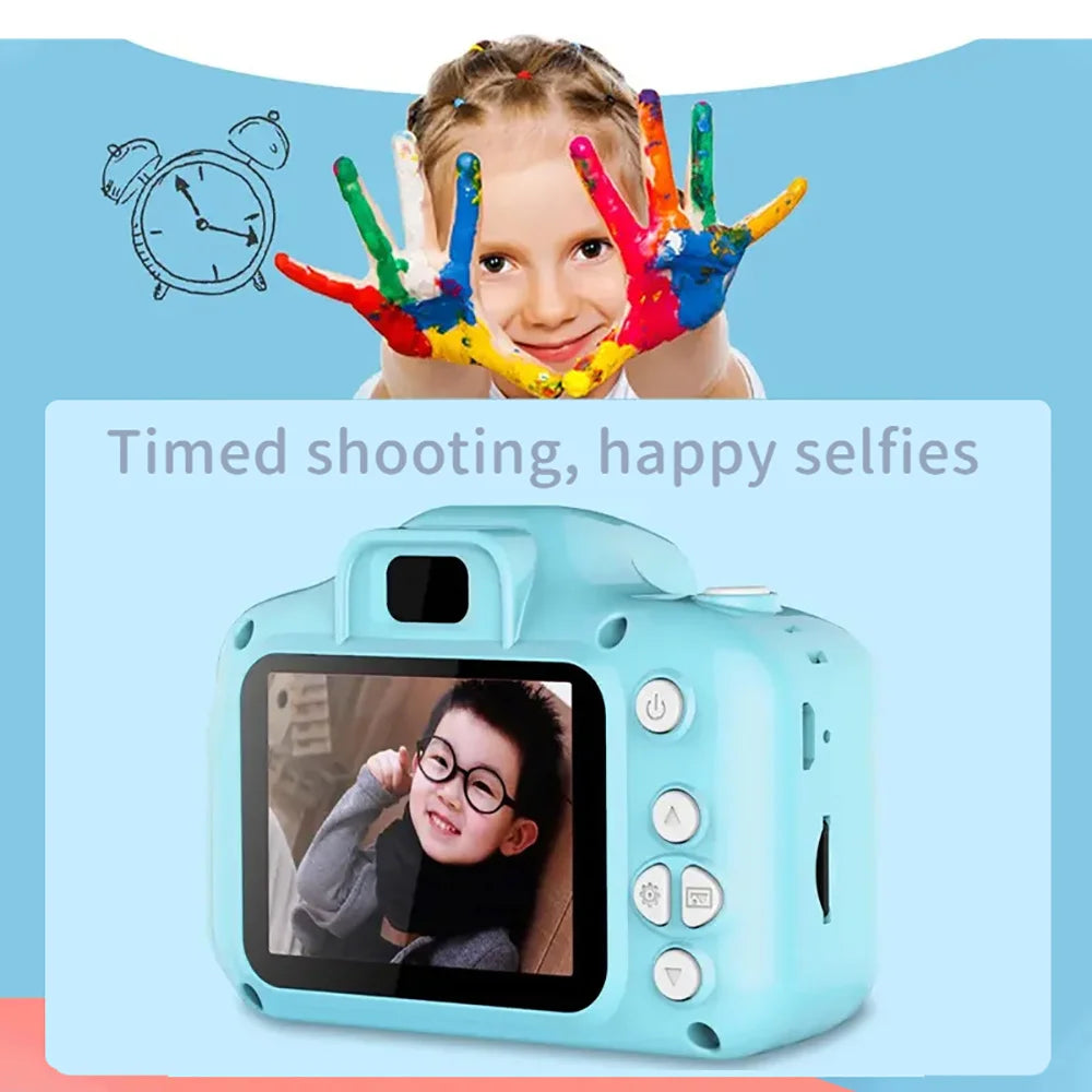 A young girl is posing for a selfie with colorful handprints in front of a small blue digital camera.