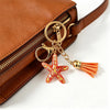 A gold-toned beaded keychain set with a starfish charm attached to a brown leather purse.