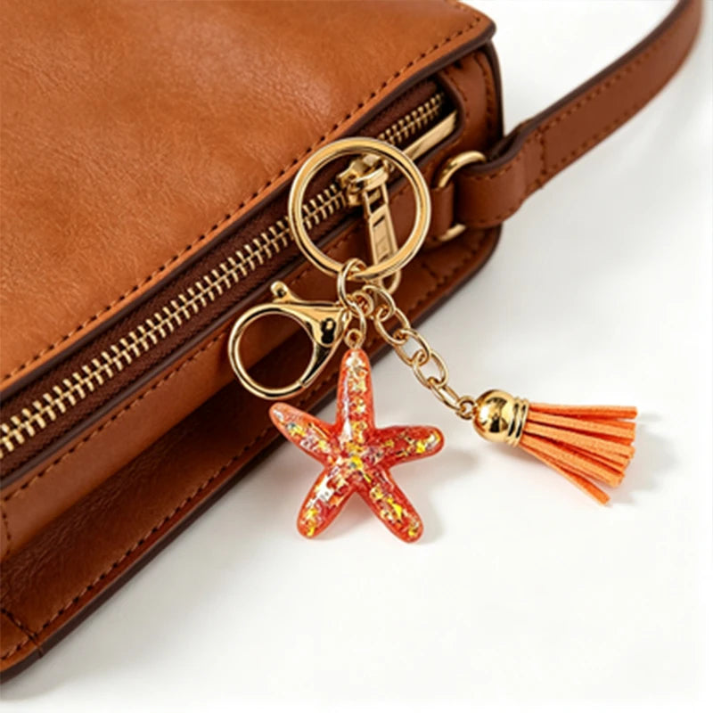 A gold-toned beaded keychain set with a starfish charm attached to a brown leather purse.