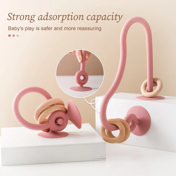 A pink silicone teething toy is shown with a hand demonstrating its strong adsorption capacity on a white surface.