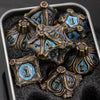 A set of seven metal dice featuring a skull and dragon design resting in a dark, textured container.