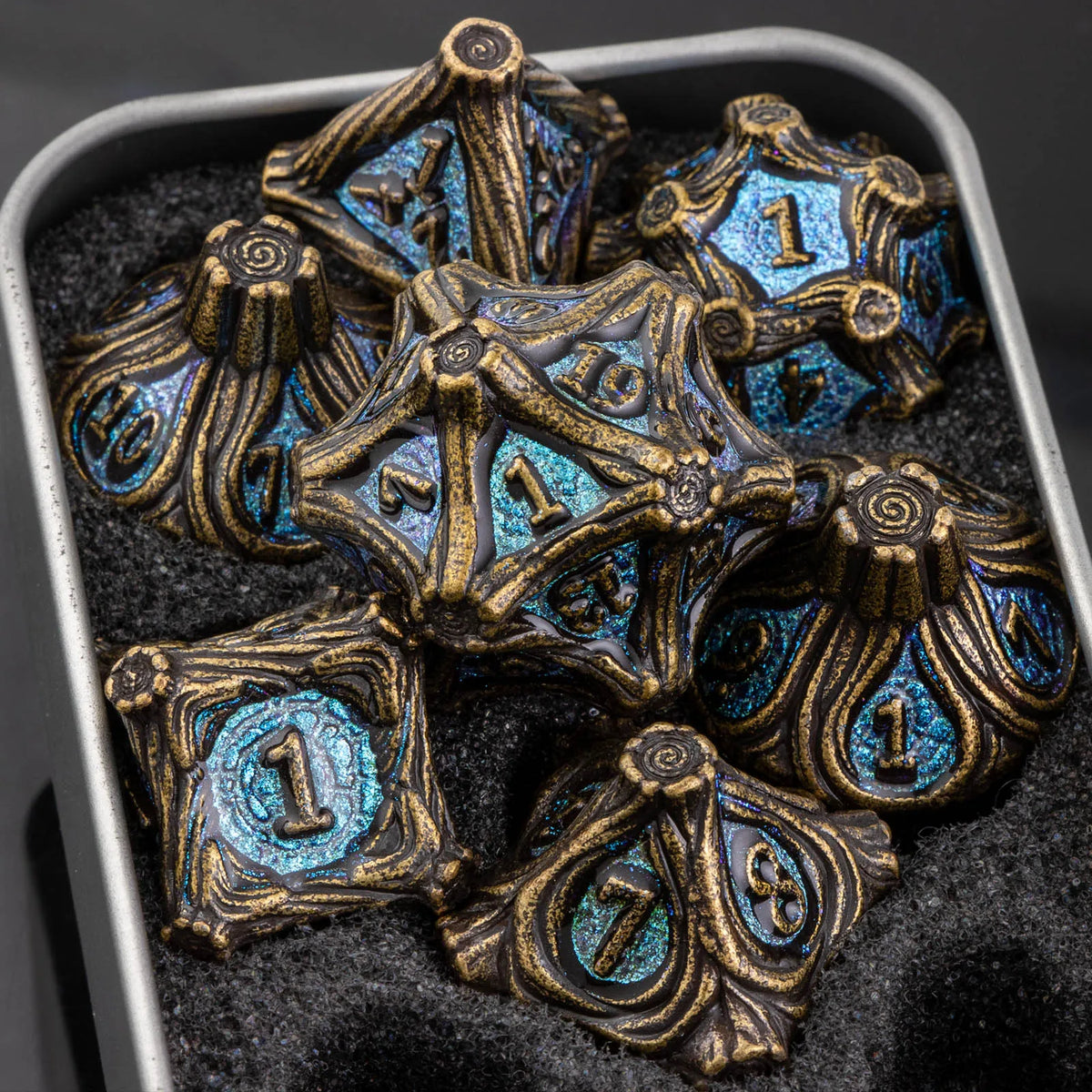A set of seven metal dice featuring a skull and dragon design resting in a dark, textured container.