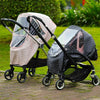 A black stroller frame is shown with a pink waterproof cover and a dark gray quilted cover in an outdoor setting.
