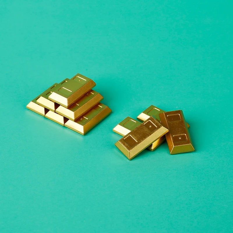 A pile of gold and silver coins arranged in a block formation on a teal surface.