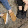 A pair of mustard yellow minimalist barefoot sneakers worn by a child on a gray rock surface.