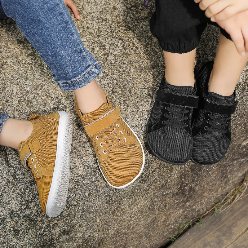A pair of mustard yellow minimalist barefoot sneakers worn by a child on a gray rock surface.