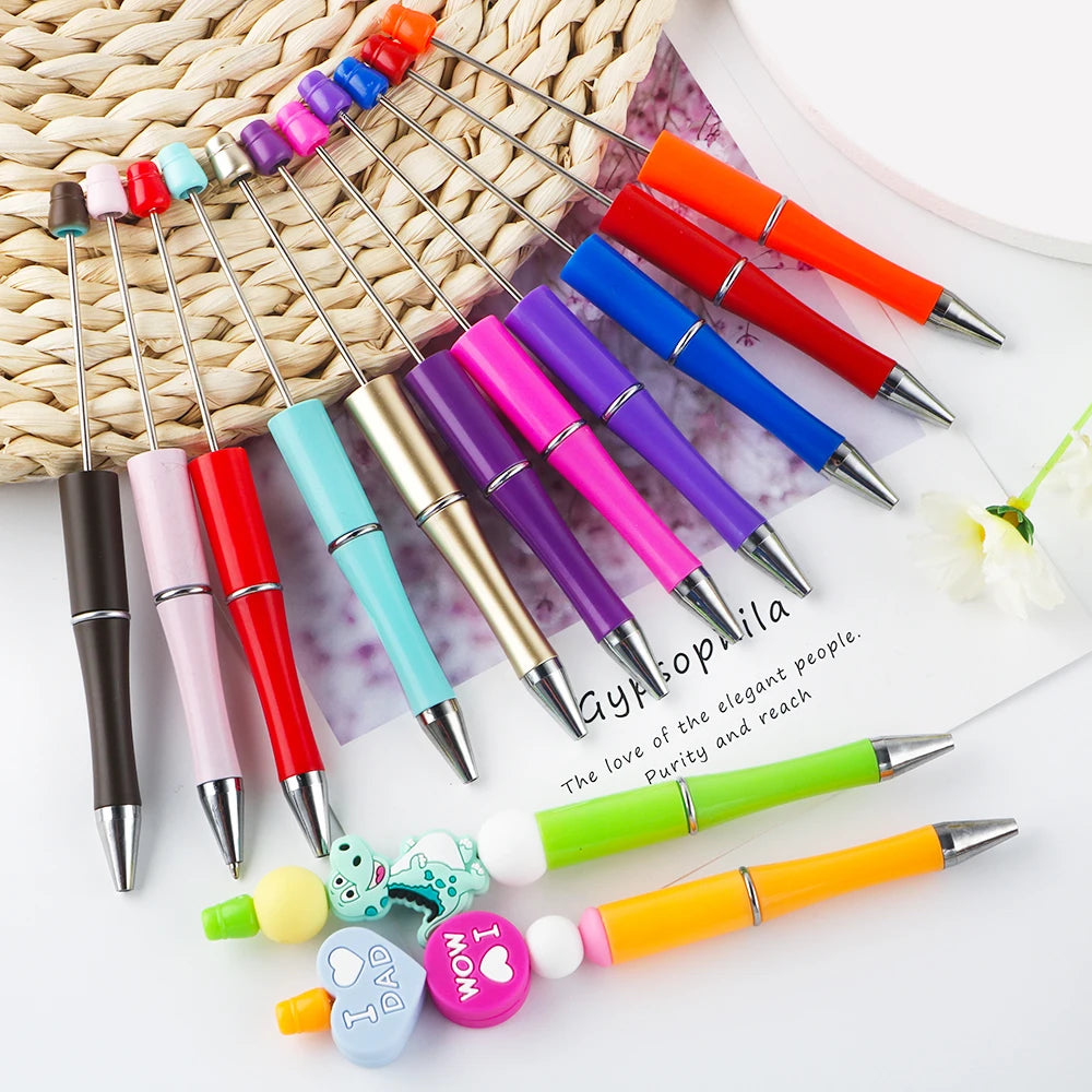 A collection of colorful beadable ballpoint pens with various tips and designs arranged on a white surface.