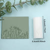 A rectangular slab of green clay featuring a detailed floral and leaf texture, next to a white cylindrical roller.