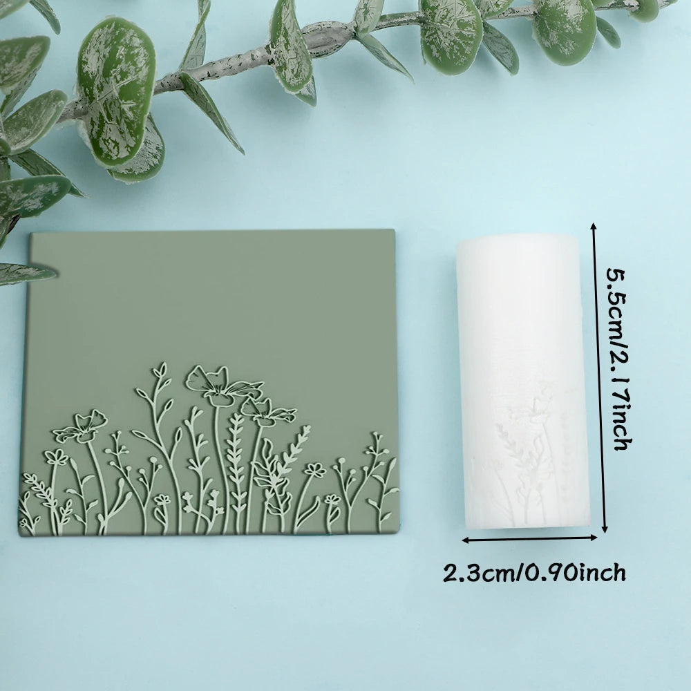 A rectangular slab of green clay featuring a detailed floral and leaf texture, next to a white cylindrical roller.