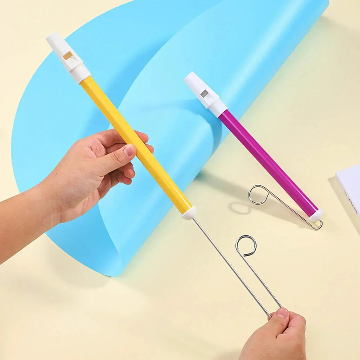 A hand holds a yellow slide whistle toy, demonstrating its use against a blue plastic slide.