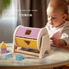 A wooden shape rolling drum toy with various colored blocks and a baby playing with it.