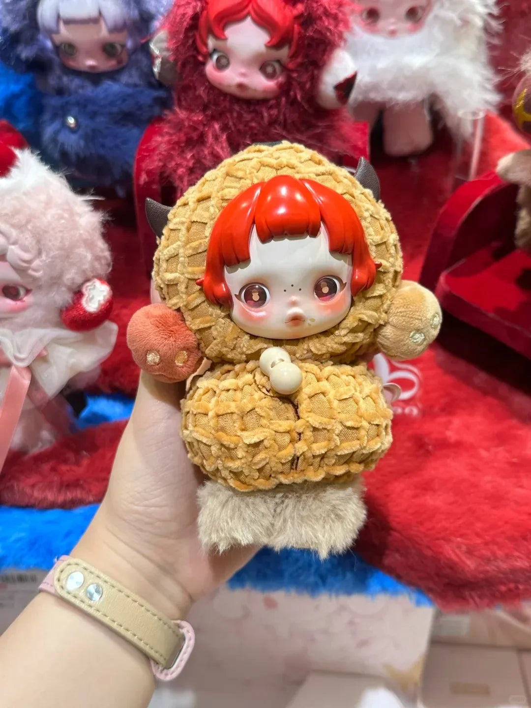 A hand holds a Skullpanda You Found Me! Series mystery box collectible figure with orange hair and a fluffy brown body.