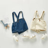 A beige denim romper for a toddler with shoulder straps and pockets, displayed on a white background.