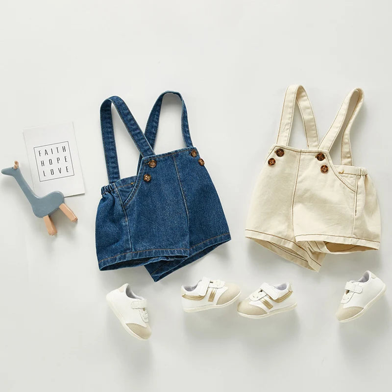 A beige denim romper for a toddler with shoulder straps and pockets, displayed on a white background.