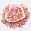 A white dish filled with colorful polymer clay sprinkles for slime and craft decor, scattered on a white background.