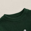 A close-up of a dark green knit sweater with white embroidery detail on the chest.