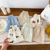 A collection of kids casual pants in various plaid and patterned fabrics laid out on a wooden surface.