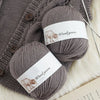 A close-up of a gray wool yarn skein with a label showing Woolyarn and an illustration of a ram.