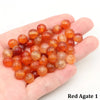 A handful of small, round, translucent orange-red agate beads resting in a person's palm.