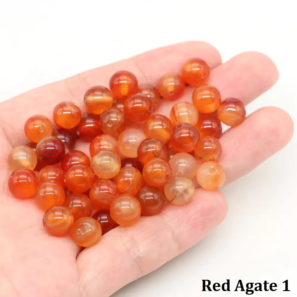 A handful of small, round, translucent orange-red agate beads resting in a person's palm.