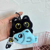 A black plush cat charm with yellow eyes and a light blue fish shape is being held by a hand.