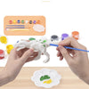 Hands paint a white dinosaur model with various colored paints and brushes on a wooden table.