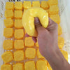 A hand is picking up a yellow squishy toy shaped like a dog noodle from a white plastic basket full of similar toys.