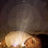 A young girl is looking at a glowing projector night light with rotating galaxy effects on her face.