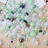 A scatter of mixed resin rhinestone pearls with an AB finish in various shades of green and clear on a wooden surface.