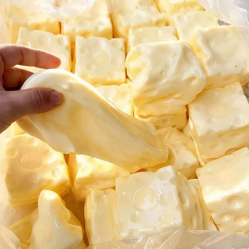 A hand holds a yellow squishy cheese cube stress ball with various shapes and textures.