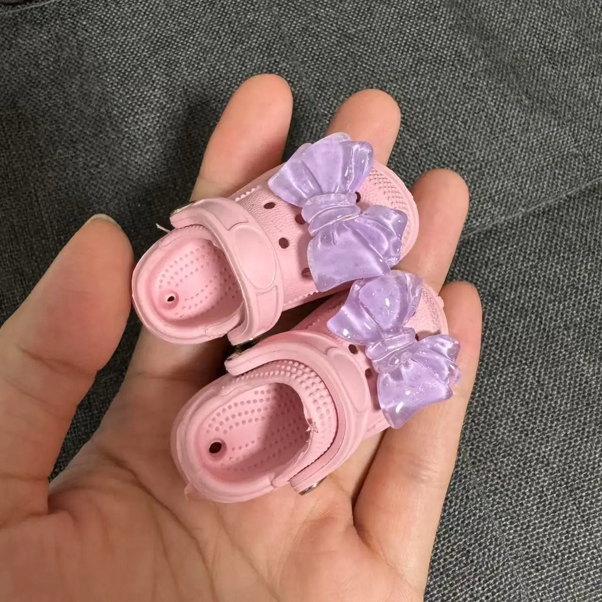 Pink fashion slippers with purple bows being held in a hand