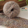 A ball of soft alpaca blend yarn with multicolored fibers resting on a knitted fabric.