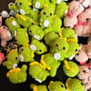 A pile of handmade crochet dinosaur keychains in various shades of green and pink.
