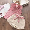 A pink floral chiffon sleeveless top and matching beige shorts set for a girl displayed on a wooden surface.