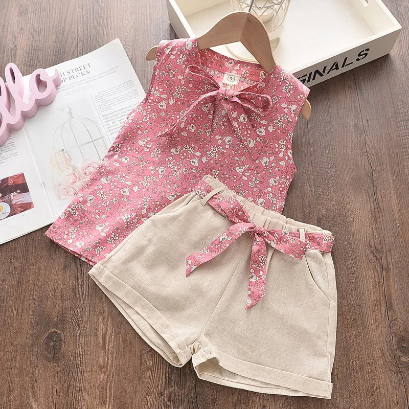 A pink floral chiffon sleeveless top and matching beige shorts set for a girl displayed on a wooden surface.