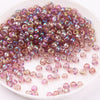 A pile of iridescent purple and pink glass rice beads for DIY jewelry and crafting.