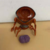 A toy replica of the Ben 10 Omnitrix Projector Watch, colored brown and orange, lying next to a purple brain model.
